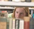 girl peering through library shelf